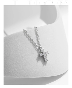 Close-up of sparkling moissanite cross pendant necklace on a clean white textured surface