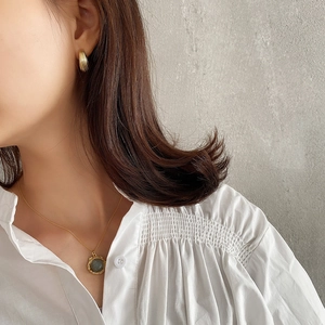 Detail of vintage gold textured hoop earrings and necklace with grey stone on white shirt