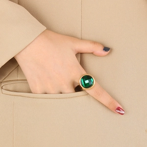 Close-up of a 22mm gold cocktail ring with a large emerald green stone on a female hand