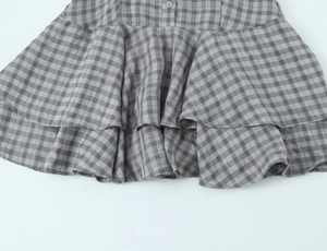 Detailed close-up of double-layered ruffle hem on a grey plaid pleated mini dress