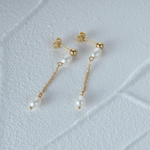 Macro shot of long gold tassel chain earrings with elegant white drop pearls