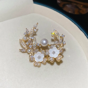 Detailed close-up of 18k gold-plated flower brooch with white pearls and shell petals