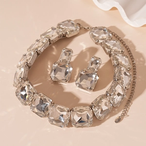 Detail of silver jewelry set featuring square-cut sparkling crystals on pink background