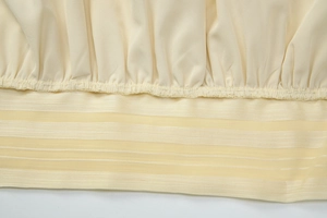 Detail of light yellow backless top featuring pleated fabric and striped mesh hemline