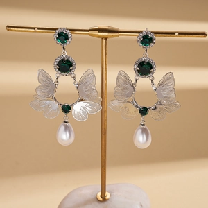 Detail of silver butterfly earrings with green stones and white pearl drops on a stand