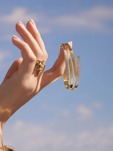 Macro shot of gold-plated spiral bangle and multi-color gemstone ring under blue sky