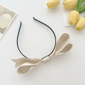 Detail of a beige satin bow headband with multiple folds on a black slim band