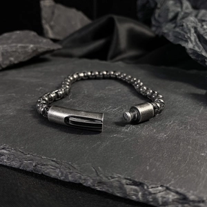 Detail of dark stainless steel beaded bracelet with cylindrical magnetic clasp on rock base