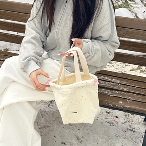 Close-up of wool dot drawstring handbag with pink rope on snowy wooden bench