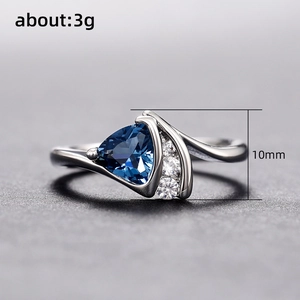 Bague en argent torsadée avec zircon bleu triangle et diamants sur fond gris mat