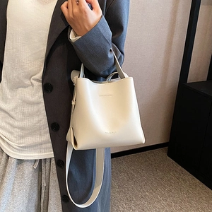 Creamy white leather bucket bag with wide shoulder strap worn by a model in grey suit
