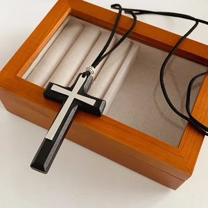 Close-up of black wood cross pendant with silver metal inlay on a wooden jewelry box