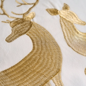 Macro detail of golden reindeer embroidery on a soft white festive pillow case fabric