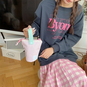 Pink checkered pencil case with green handle held by hand in a cozy lifestyle setting