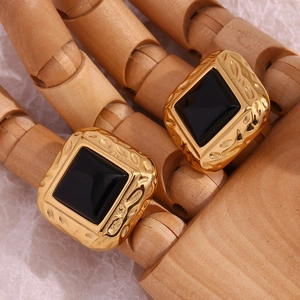 Macro view of vintage hammered gold square studs with black acrylic inlay on a wooden hand