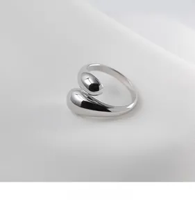 Macro shot of silver polished water drop open ring on white silk textured background