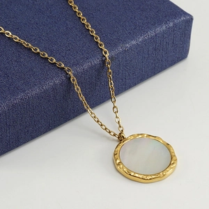 Close-up of a 18K gold-plated shell pendant necklace displayed on a navy blue gift box