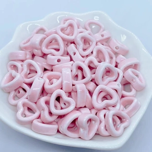 Close-up of pink heart-shaped ceramic beads with hollow centers in a white petal dish