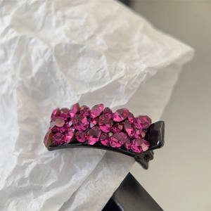 Détail d'une petite pince à cheveux noire avec des strass roses brillants sur papier plissé