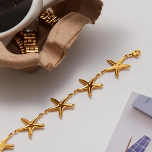 Detail view of 18K gold plated stainless steel bracelet with starfish charms on white surface