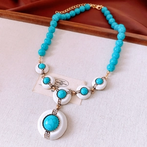 Détail macro du collier de perles turquoise avec pendentif blanc et touches dorées