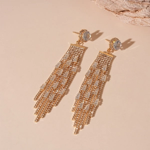 Detail of luxury gold tassel earrings with sparkling white crystals on a wooden stand