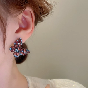 Close-up of vintage butterfly stud earrings featuring red and blue zircon on a model ear