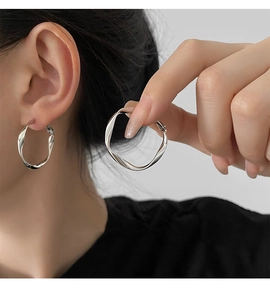 Close-up of a model wearing large silver twisted geometric hoop earrings in a minimalist style