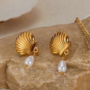 Detail of gold shell earrings with white teardrop pearl drops on a natural stone surface