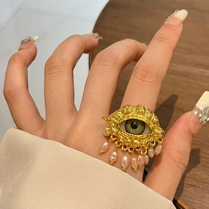 Detail of vintage gold evil eye ring with green eye stone and pearl drop charm on hand
