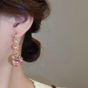 Close-up of heart-shaped pink zircon earrings with colorful stones on a female model