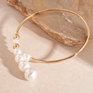 Elegant gold open cuff bracelet with white faux pearls on a textured stone background