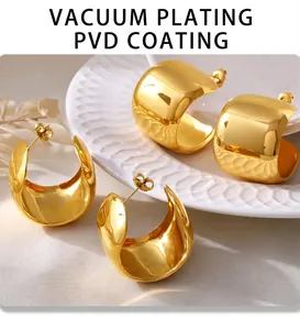 Close-up of golden PVD coated C-shaped wide earrings on a textured ceramic surface