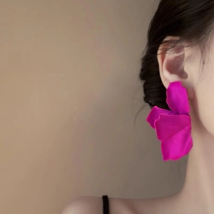 Detail of oversized magenta petal earrings worn by a model against a beige background