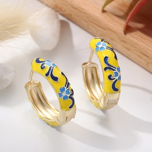 Detailed view of yellow enamel hoop earrings with blue floral patterns on a stone background