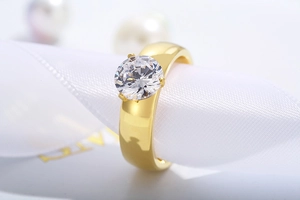 Macro shot of a gold titanium ring with a round 6mm solitaire zircon on white satin ribbon