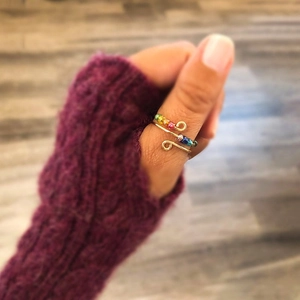Detailed shot of handmade gold wire ring with rainbow beads on a model wearing purple gloves