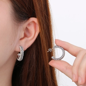 Close-up of C-shaped stainless steel earrings with white faux pearls on model and in hand