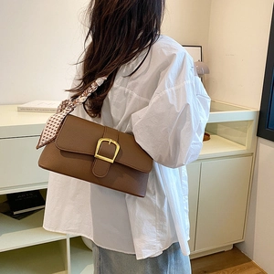Brown leather baguette bag featuring a gold buckle and silk scarf on the shoulder strap