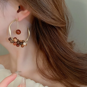 Detail of C-shaped boho hoop earrings with colorful wooden beads on a model's ear