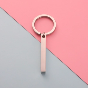 Polished rose gold stainless steel cuboid pendant keychain on a minimalist background