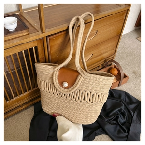 Detail of khaki straw woven tote bag featuring a brown leather flap and pearl clasp
