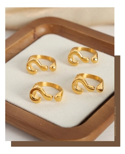 Detailed view of four golden question mark rings on a minimalist beige jewelry tray