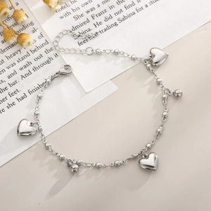 Close-up of silver beaded heart anklet on book page with dried flowers and lobster clasp