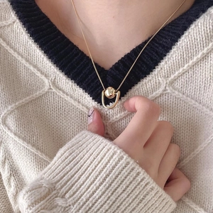 Close-up of a minimalist golden U-shaped bead necklace worn on a white knit sweater
