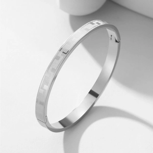 Titanium steel bangle with Greek key pattern and secure clasp on a minimalist background