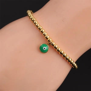 Detail of gold beaded bracelet with green evil eye enamel charm on a wrist