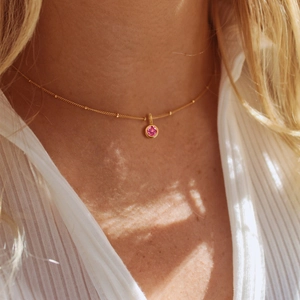 Gold chain necklace with pink birthstone pendant and small metal beads worn by a model