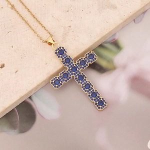 Golden cross necklace with inlaid blue round gemstones on a textured stone surface