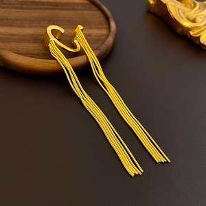 Detailed close-up of golden tassel ear cuff earrings on a wooden tray with metallic shine